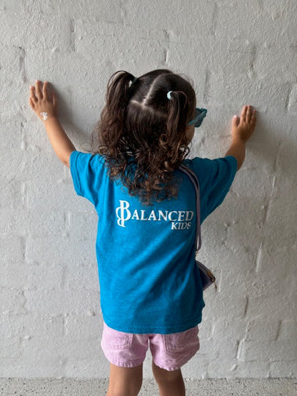 Child wearing a bright blue B.Balanced Co. crew neck t-shirt with white Balanced Kids logo on the back