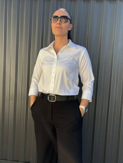 Female standing front on in a white button up shirt and black pants with black belt